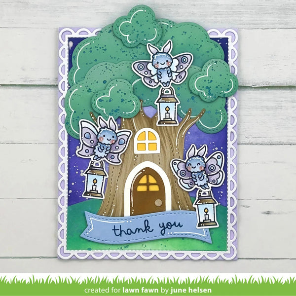A decorative handmade greeting card featuring a whimsical fairy treehouse scene with three blue-and-white fairy characters, lanterns, a brown tree trunk, green leaves, and a purple night sky. The card has a scalloped white border and a blue banner reading “thank you.