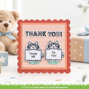 A handmade square greeting card with a scalloped rust-orange border, featuring two cartoon cats holding signs that read 'FROM ME' and 'TO YOU' beneath the text 'THANK YOU!'. The card is styled on a tabletop with a teddy bear and gift boxes in the background.