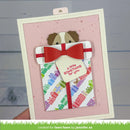 A handmade greeting card featuring a small dog illustration above a gift bag with a red bow and the phrase 'a little SOMETHING for you.' The card is held in a hand against a light gray wood-plank background.