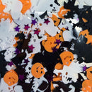 A close-up of Halloween-themed flat confetti pieces scattered together, including white ghosts, black bats and jack-o'-lanterns, orange pumpkins, and purple stars.