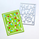 A handmade greeting card with a bright green background, white border, and colorful Christmas light bulbs, shown next to a silver metal die-cutting template on a white background.
