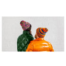 Two people wearing colorful beanies and reflective jackets standing against a white brick wall.