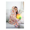 Child wrapped in a colorful blanket on a couch holding a ball