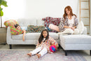 Woman and two children sitting on a couch with colorful pillows in a living room.