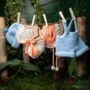Crocheted baby hats and overalls hanging on a line with a natural background.