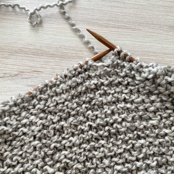 Knitted fabric with wooden knitting needles on a light wooden surface