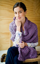 Woman wearing a purple knitted shawl sitting on a wooden chair.