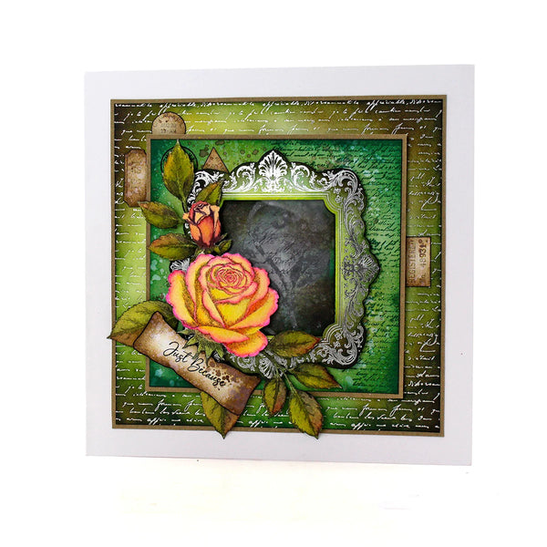 A square handmade greeting card featuring a vintage-style floral design with a large yellow and pink rose, smaller rosebud, green leaves, an ornate silver frame, and a banner reading 'Just in Time'. The card has a layered collage design with a green background, cursive script, and textured details, presented on a clean white background.