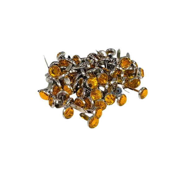 A pile of small oval amber-yellow rhinestones with silver metal settings and backing pins, photographed on a plain white background.