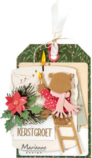 A layered Christmas greeting card or craft tag design with a hanging ribbon, green patterned backing, cream and beige paper layers, a red poinsettia, green holly, pine branches, a small bear figure in a red polka-dot outfit, and the text 'KERSTGROET' and 'Marianne design'.