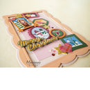 A handmade layered Christmas greeting card with scalloped peach borders, featuring colorful holiday embellishments, a gold 'Merry Christmas' script, and small photo frames on a light cream background.