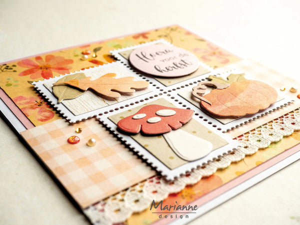 A close-up of a handmade autumn-themed card featuring layered scrapbook papers, die-cut leaf and mushroom shapes, floral accents, and a small circular tag reading 'Here we go.