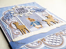 A close-up of a handmade layered greeting card featuring Peter Rabbit in the snow with two deer cutouts, blue and white scalloped borders, and the text 'FINE KERST' and 'Marianne design'.