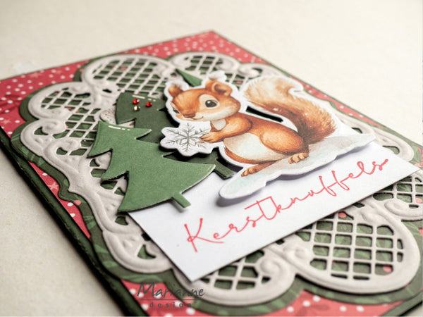 A handmade Christmas card featuring a die-cut illustration of a brown squirrel holding a white snowflake, layered over a green Christmas tree silhouette and a white scalloped paper border. The card has a red and white polka-dotted background and a white card at the bottom with the German text 'Kerstinuffels' in red script.