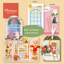 A collage of Christmas-themed paper craft or scrapbook kit cards and templates from Marianne Design, including arched window cutouts, floral and rustic tags, a small doll figure, and decorative labels, with the text 'Christmas coziness' in the center.