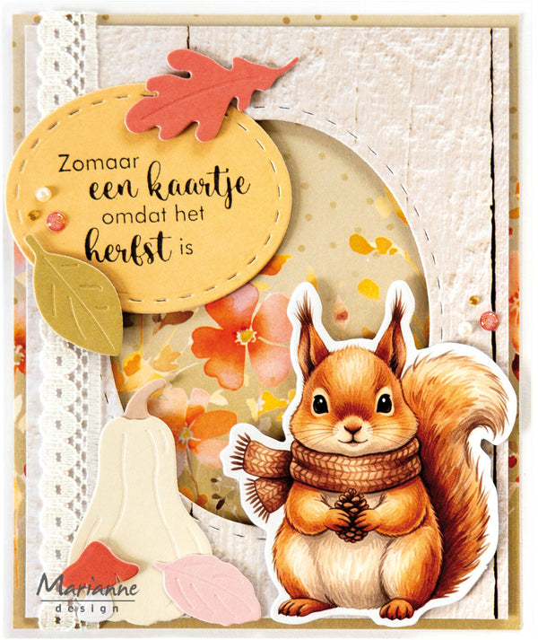 A handmade autumn-themed card featuring a die-cut illustration of a brown squirrel wearing a brown scarf, layered over floral and leaf embellishments, with a yellow tag containing Dutch text and the brand name 'Marianne design' in the lower left corner.
