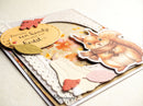 A close-up of a handmade layered greeting card featuring a cute illustrated squirrel wearing a scarf, autumn leaves, lace, and a circular card with Dutch text, photographed on a light neutral background.