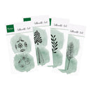 Three packages of Marina's Creations Silhouette Art clear stamps fanned out on a white background. The packages feature green watercolor wash designs with black line drawings of Christmas ornaments, a pine tree, foliage, and a pine branch.