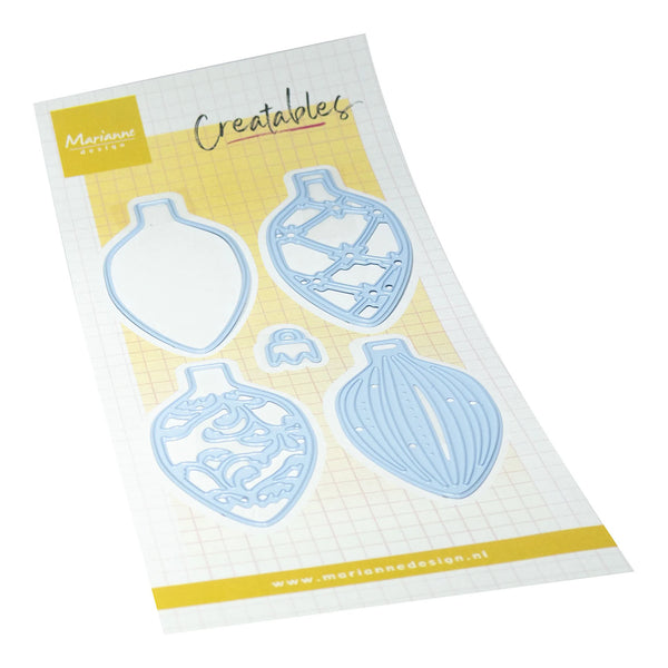 A sheet of craft dies from Marienbadesign Creatables, featuring four ornate Christmas ornament-shaped metal dies in light blue on a white grid background with yellow accents.