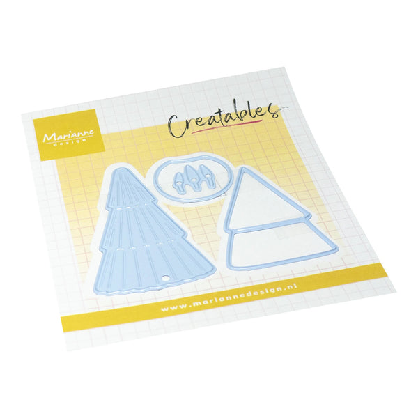 A Marianne Design 'Creatables' die-cut craft set on a white grid backing card with yellow accents. The set includes two light blue plastic templates shaped like a Christmas tree and a house, with a small oval piece showing three small figures.