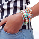 Colorful beaded bracelets on a wrist with a striped shirt and jeans in the background