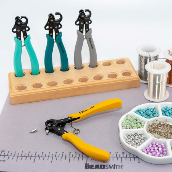 Jewelry-making tools including pliers and a stand on a table with beads and wire.