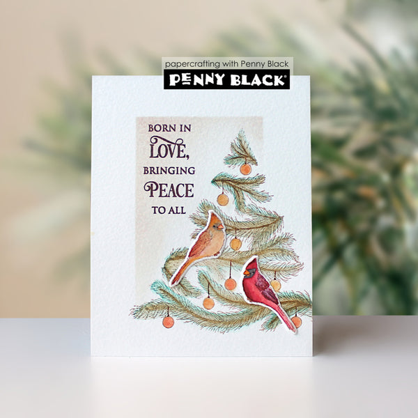 A handmade greeting card featuring a watercolor-style Christmas tree with two cardinals, orange ornaments, and the text 'BORN IN LOVE, BRINGING PEACE TO ALL'. The card is displayed upright on a white surface with a soft-focus background.
