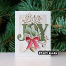A handmade greeting card featuring a large layered green 'JOY' letter with green leaves, red berries, and a red bow, displayed against a blurred green pine background. A 'pencrafting with Penny Black PENNY BLACK' brand label is visible at the bottom of the card.