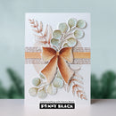 A handmade greeting card featuring a layered paper bow and botanical elements in muted green, beige, and brown tones, with a visible Penny Black brand label at the bottom.