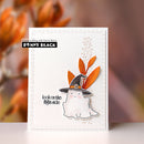 A handmade greeting card featuring a cute white ghost wearing a black witch hat with orange leaves on top, set against a blurred warm orange background. The card has a white embossed border and the text 'look on the bright side' next to the Penny Black logo.