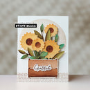 A handmade greeting card featuring layered paper sunflowers with green leaves and a brown banner that reads 'Gratitude'. The card is displayed on a neutral, softly blurred background with a 'Penny Black' brand label visible in the top left corner.