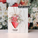 A handmade Christmas greeting card by Penny Black, featuring a textured white card base with a red watercolor heart, a pink poinsettia, green leaves, and a gold bow, set against a blurred floral background.