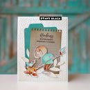 A handmade greeting card by Penny Black featuring a layered autumn-themed design with a child holding a rake, small birds, leaves, and a kraft paper insert with the phrase 'Kindness Scatters Beauty Whenever It Is Shared.' The card is photographed standing upright against a blurred turquoise wooden background.
