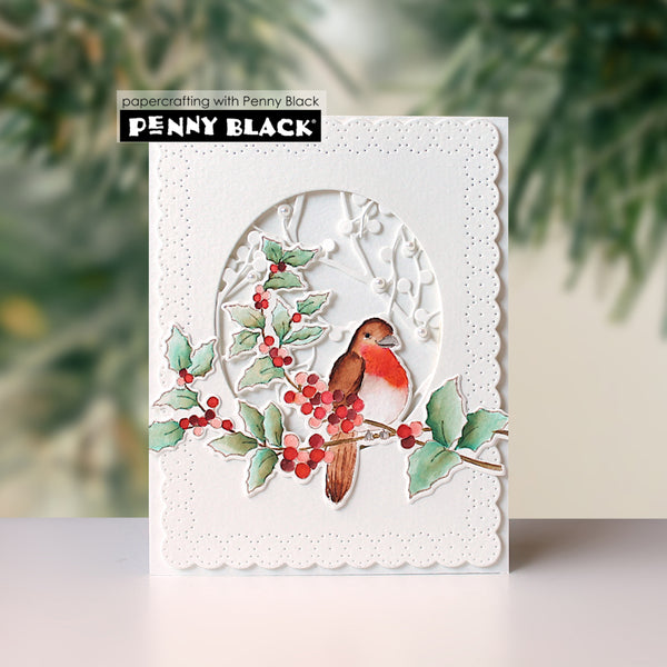 A handmade greeting card by Penny Black featuring a white scalloped border and a die-cut oval design with a bird, holly leaves, and red berries. The card is displayed on a light surface with a blurred green pine background.