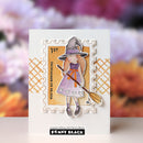 A handmade greeting card featuring a die-cut illustration of a witch holding a broomstick, styled with a stamp-like border and the text 'YOU'RE SO BEWITCHING' and '1ST'. The card is displayed against a blurred floral background, with the Penny Black logo visible at the bottom.
