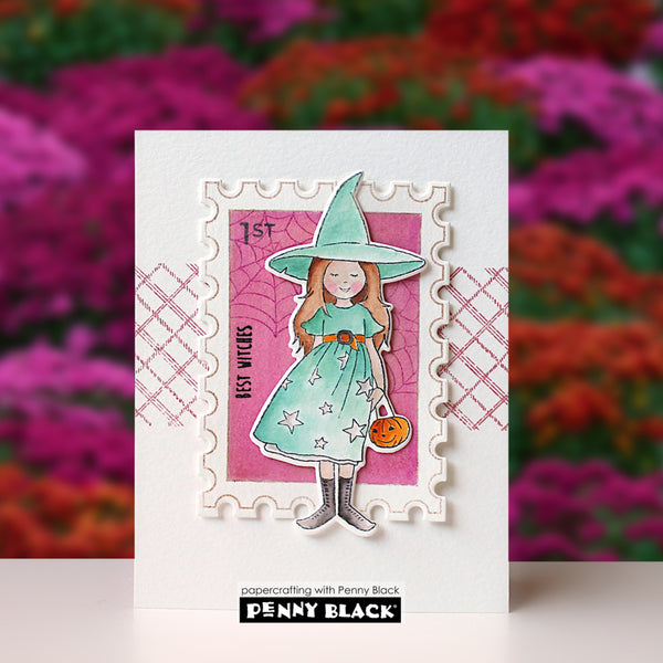 A handmade greeting card featuring a die-cut stamp design of a witch in a teal dress and hat against a pink spiderweb background, with decorative patterned borders and a visible Penny Black brand mark at the bottom.