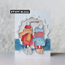 A handmade greeting card featuring two children from behind wearing winter coats and scarves, with the text 'spirits bright' on the card. The card is branded with 'Penny Black' and 'papercrafting with Penny Black' text, set against a soft, textured gray background.
