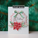 A handmade layered Christmas greeting card by Penny Black, featuring a white embossed background, a pink scalloped arch, a mint green bow, red poinsettias, holly leaves, and the words 'Warm Wishes'.