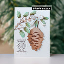 A handmade holiday greeting card featuring a dimensional copper pinecone, green holly leaves, berries, and a white ribbon bow, with a black stamp brand label reading 'Penny Black' at the top.