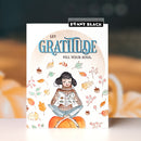 A vertical greeting card featuring a watercolor illustration of a girl reading on a pumpkin, surrounded by autumn leaves and acorns, with the text 'LET GRATITUDE FILL YOUR SOUL.' The card is branded with 'Penny Black' at the top, set against a blurred warm-toned background.