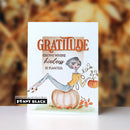 A handmade greeting card featuring a watercolor illustration of a woman sitting on a pumpkin with the text 'GRATITUDE GROWS WHERE kindness IS PLANTED.' The card is displayed upright against a blurred autumn leaf background, with a 'Penny Black' brand label at the bottom left.