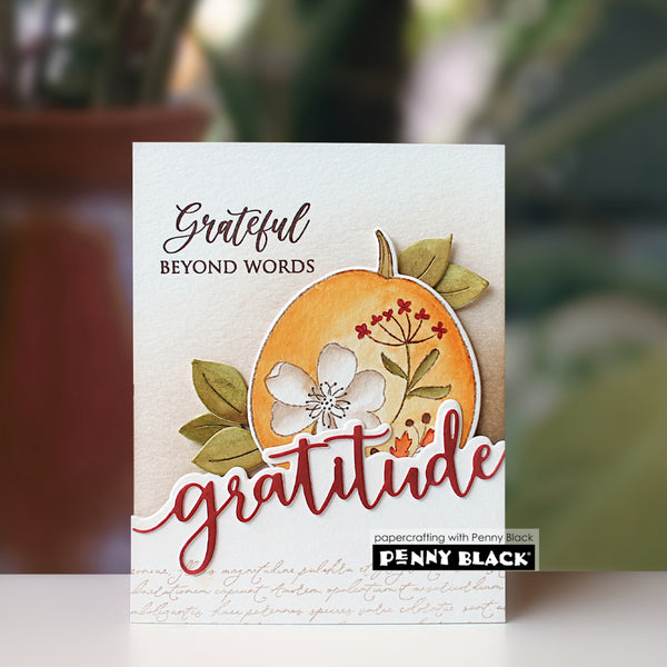 A handmade greeting card featuring a layered autumn design with a stamped orange pumpkin, white flower, green leaves, and the words 'grateful beyond words' and 'gratitude'. A small brand label at the bottom reads 'papercrafting with Penny Black' and 'PENNY BLACK'.