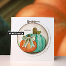 A handmade circular card featuring an embroidered pumpkin design in orange and teal with a mint green bow, displayed on a white cardstock with a scalloped edge. The card is set against a blurred background of pumpkins, with a 'Penny Black' brand label overlay on the left.