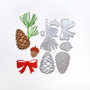A set of autumn-themed crafting dies and finished sample pieces on a white background, including pinecones, acorns, a green pine branch, a red bow, and metal templates for shapes like a bird, acorn, and acanthus leaf.