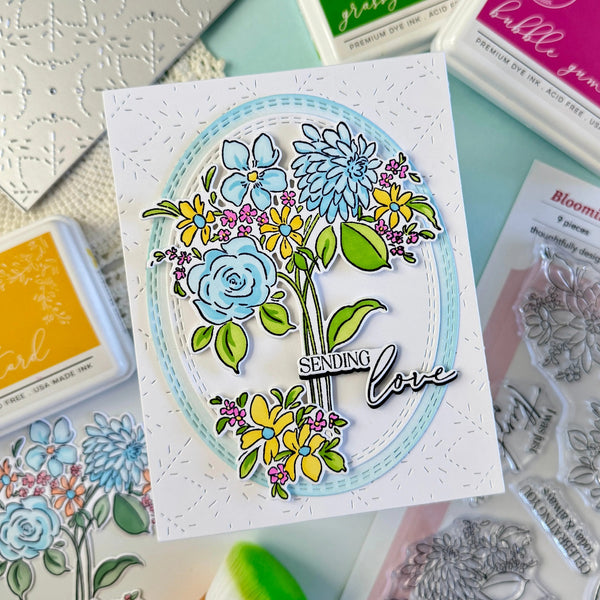 Card with floral design and 'Sending love' text, surrounded by stamping tools on a light blue background.
