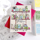 A handmade Christmas-themed card featuring illustrated shelves with houses, stars, a tree, books, ornaments, gifts, and a deer, with the text 'Wishing you a season to Treasure.' The card is styled with red and pink paper, clear stamp sheets, and Ranger Ink premium inks on a white background.