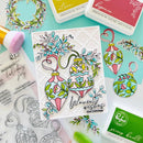 A handcrafted Christmas card featuring two colorful ornament illustrations with floral details and the text 'Warmest wishes this Christmas,' styled on a mint background with ink pads, stamps, and brushes.