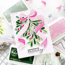 A handmade layered card featuring a large pink ribbon bow, green mistletoe with pink berries, and the text 'Let your heart be merry' on a white background, surrounded by Stampfing Ink products and holiday decorations.