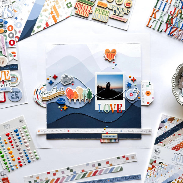 Scrapbooking layout with cut-out letters, stickers, and a photo of a couple on a white surface.