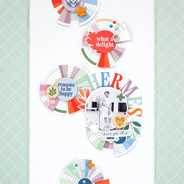 A collection of colorful scrapbook paper circles and layered paper designs arranged on a white background, featuring retro text like 'what a delight', 'reasons to be happy', and 'HERMES', alongside small illustrations and pastel patterned accents.